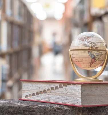 A small globe on a book placed in a library with blurry bookshelves in the background.