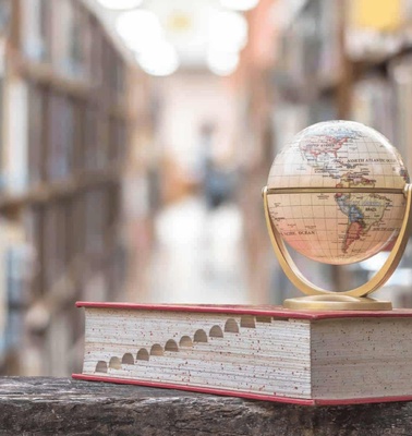 A small globe on top of a book in a library aisle.