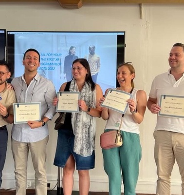 A group of seven people happily posing with certificates in a room with a projector screen in the background.