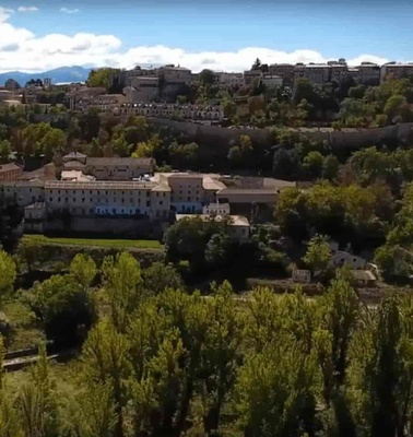 Aerial view of a historical town with stone walls, featuring dense greenery and old architectural structures.