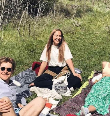 Three people relaxing and enjoying a sunny day on a picnic blanket in a grassy field.