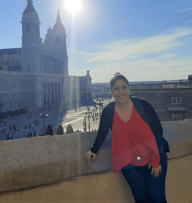 A woman smiling in front of a historic building on a sunny day.