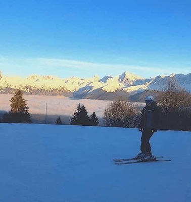 A skier stands on a snowy slope with a panoramic view of distant mountains under a clear blue sky.