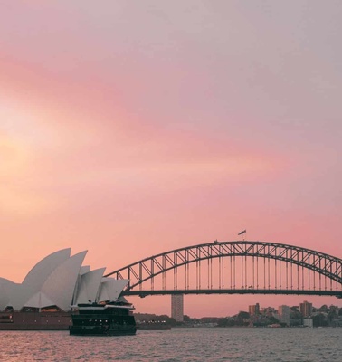The Sydney Opera House and Harbour Bridge pictured against a pink sky at sunset.