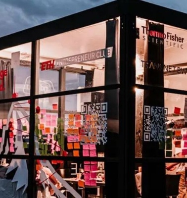 A modern glass structure filled with colorful sticky notes and illuminated during sunset.