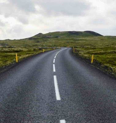 A scenic open road leading through a green landscape under a cloudy sky.