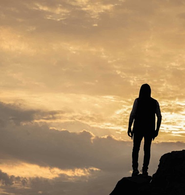 Silhouette of a person standing on a rock against a sunset sky.