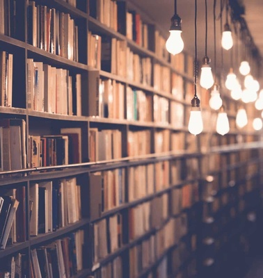 A dimly lit library aisle with rows of books on wooden shelves and hanging lights.