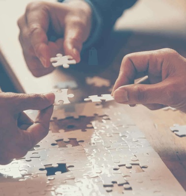 Two people assembling a jigsaw puzzle on a wooden table.