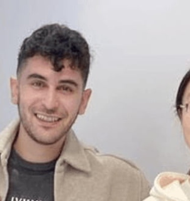 Four young adults smiling and standing close together in an indoor setting.