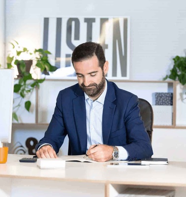 A man in a suit is writing in a notebook at an office desk.