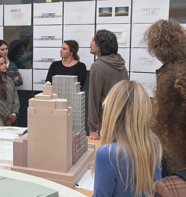 A group of people attentively listening to a presentation about architectural models and designs.