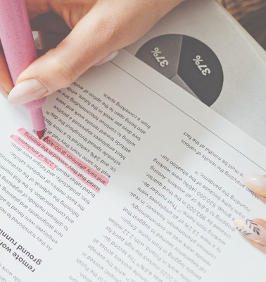 A person highlighting text on a printed document with a pink highlighter.