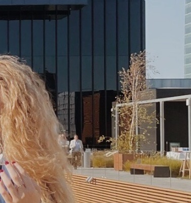 Three women smiling and standing together in front of a modern building with glass facade and a water feature.