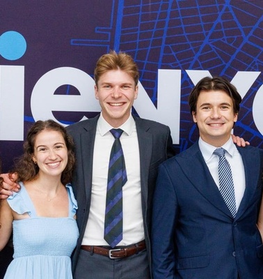A group of young adults pose together in front of a purple backdrop featuring a map design.