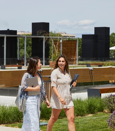 Two women are walking together outdoors in a modern park setting.