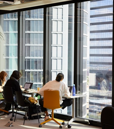 People working in a modern office space with large windows overlooking a cityscape.