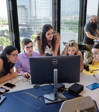 A group of young people collaborating around a computer in a modern office space.