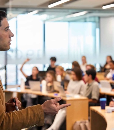 A man gives a lecture to a classroom full of engaged students.
