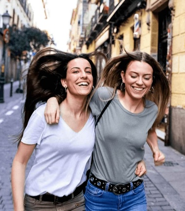 Two women happily walking arm in arm on a city street.