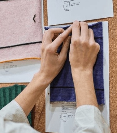 A person is attaching a purple fabric swatch to a corkboard with pinned documents.
