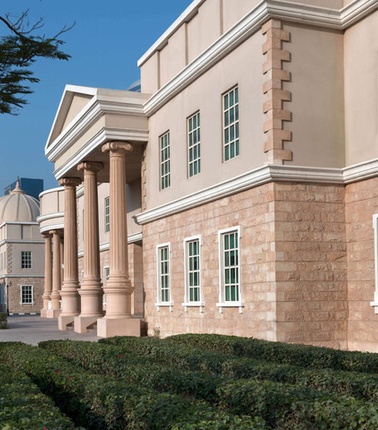 This image depicts an elegant building featuring classical architectural elements and green hedges in the foreground.