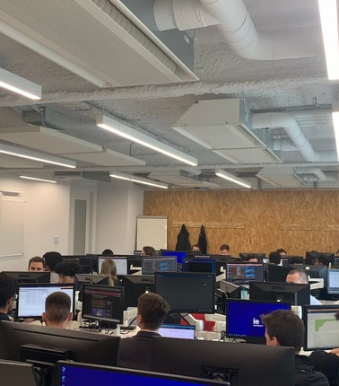 A modern office environment with numerous people working at computer desks.
