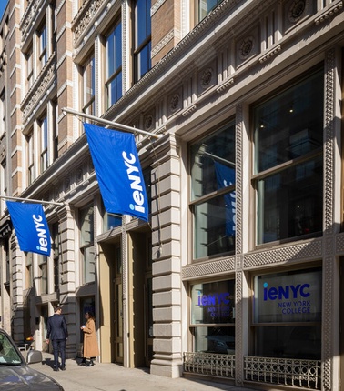 A modern building facade with blue flags displaying 'ieNYC' in a city setting.