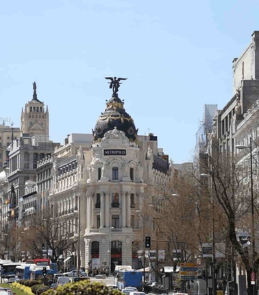 A bustling urban scene showcasing a grand building with a statue on top, and a busy street filled with cars.