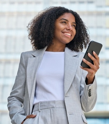 A woman in a light gray suit smiles while holding a smartphone.