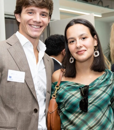 A smiling young man and woman attending a social event, both dressed in smart casual attire.