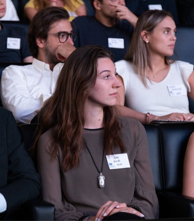 A group of young adults attentively sitting at an event, wearing name tags.