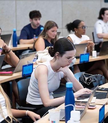 A group of students attentively working on laptops in a classroom setting.