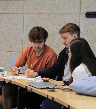A group of students collaborating on a project at a table with a laptop and notes.