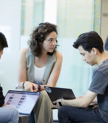 A group of people discussing and working on laptops in a modern office setting.