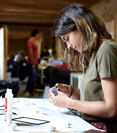 A young woman is focused on crafting at a well-lit workspace.