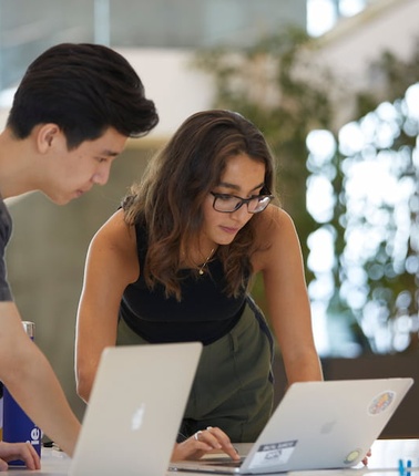 Two individuals are collaborating over laptops in a modern workspace.