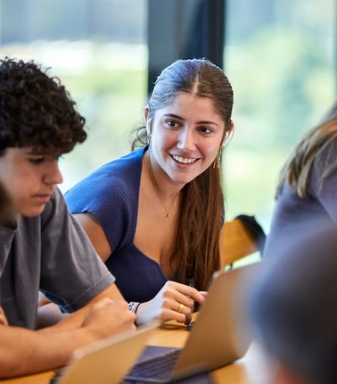 A group of young people engaged in a discussion at a table, with one person smiling.