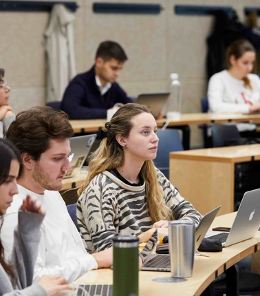 A group of students attentively participating in a classroom setting with laptops.