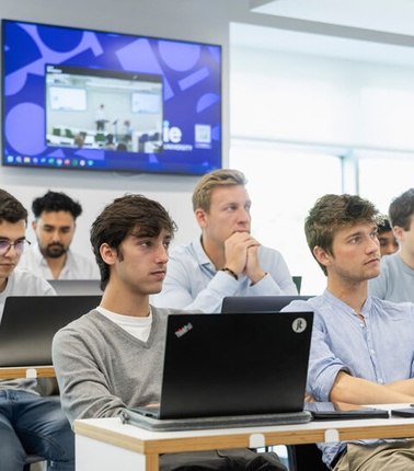 A group of students attentively listening in a modern classroom setting.