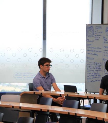 A student is writing on a whiteboard while another student sits and observes in a classroom.