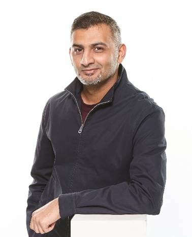 A man in a dark zip-up jacket smiling at the camera against a white background.