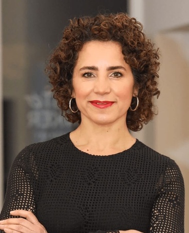 Portrait of a middle-aged woman with curly hair, wearing a black mesh top and smiling.