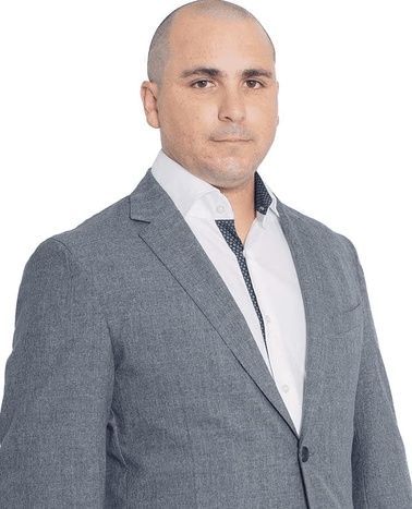 A bald man in a gray suit and white shirt posing against a plain background.