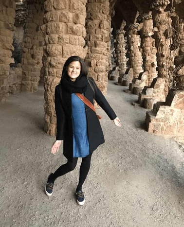 A woman smiling and posing between tall stone columns in an ancient, historical site.