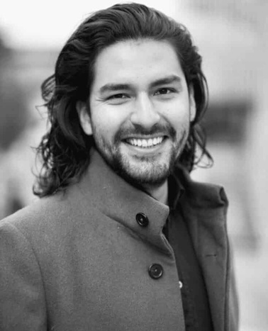 Black and white portrait of a smiling man with long hair wearing a peacoat.