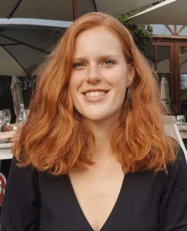 A smiling woman with red hair sitting at an outdoor setting