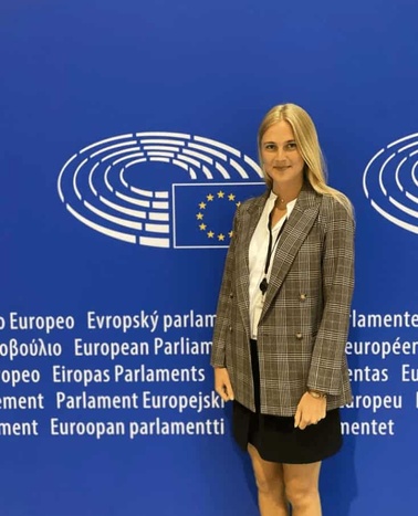 A woman in a business suit standing in front of the European Parliament logo.