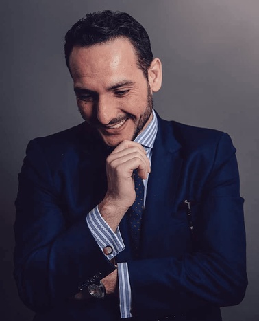 A smiling man in a blue suit and striped tie looking at his hand thoughtfully.