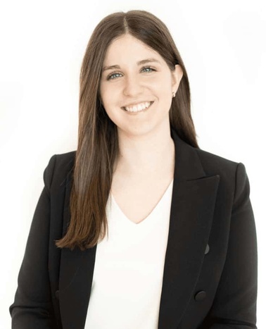 A professional portrait of a smiling woman wearing a black blazer over a white top against a white background.